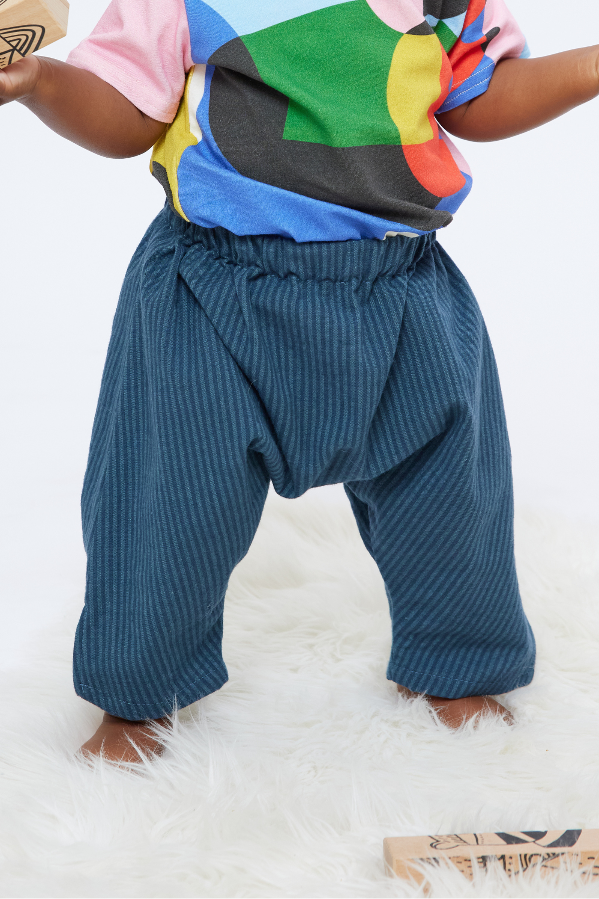 baby standing on a furry rug wearing gender neutral stipe pants